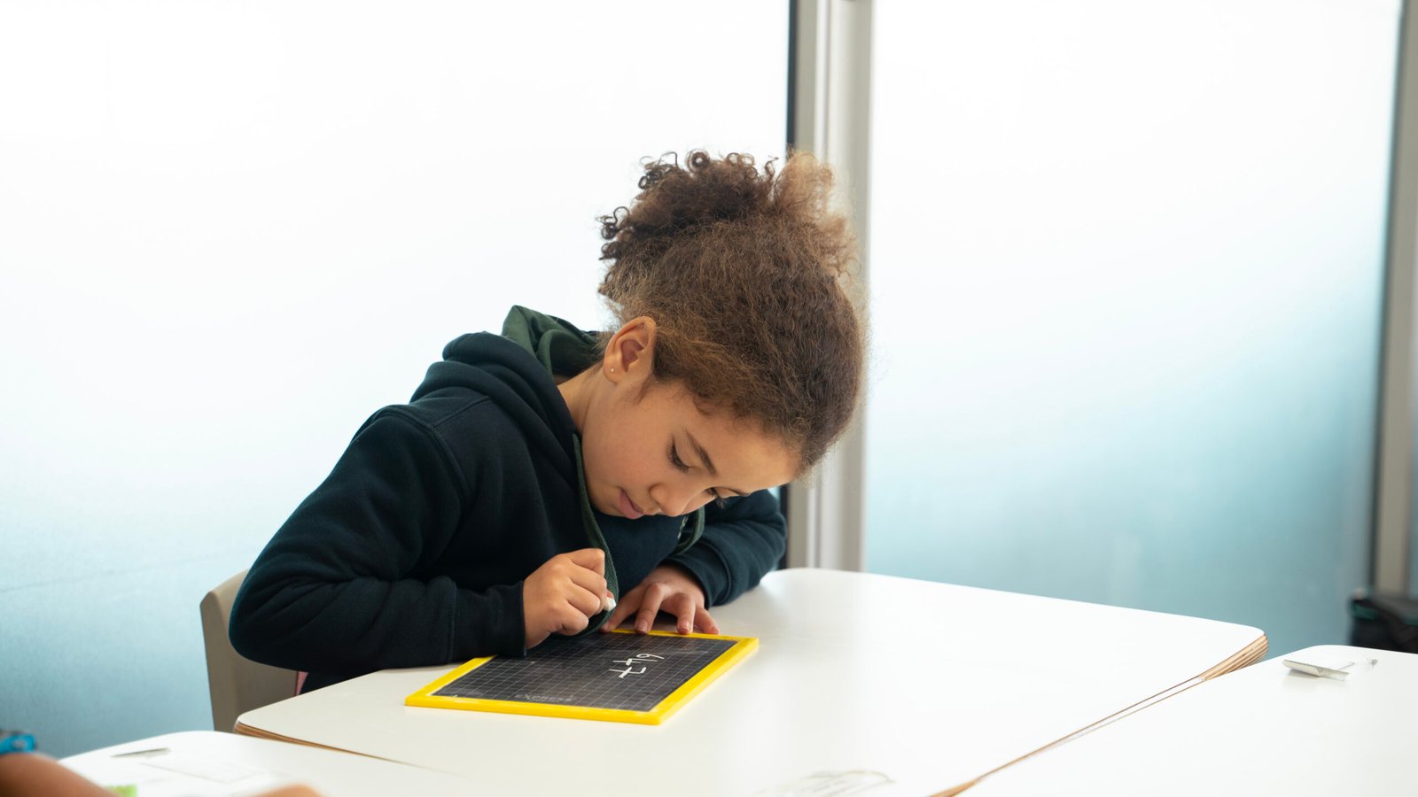 Une jeune fille écrit sur un tableau noir avec un marqueur jaune, en tant qu'élève à l'école.